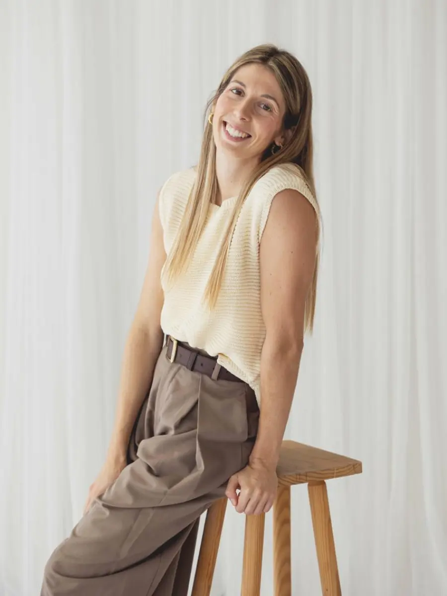 Ana González, psicóloga, apoyada en un taburete de madera y sonriendo con calidez