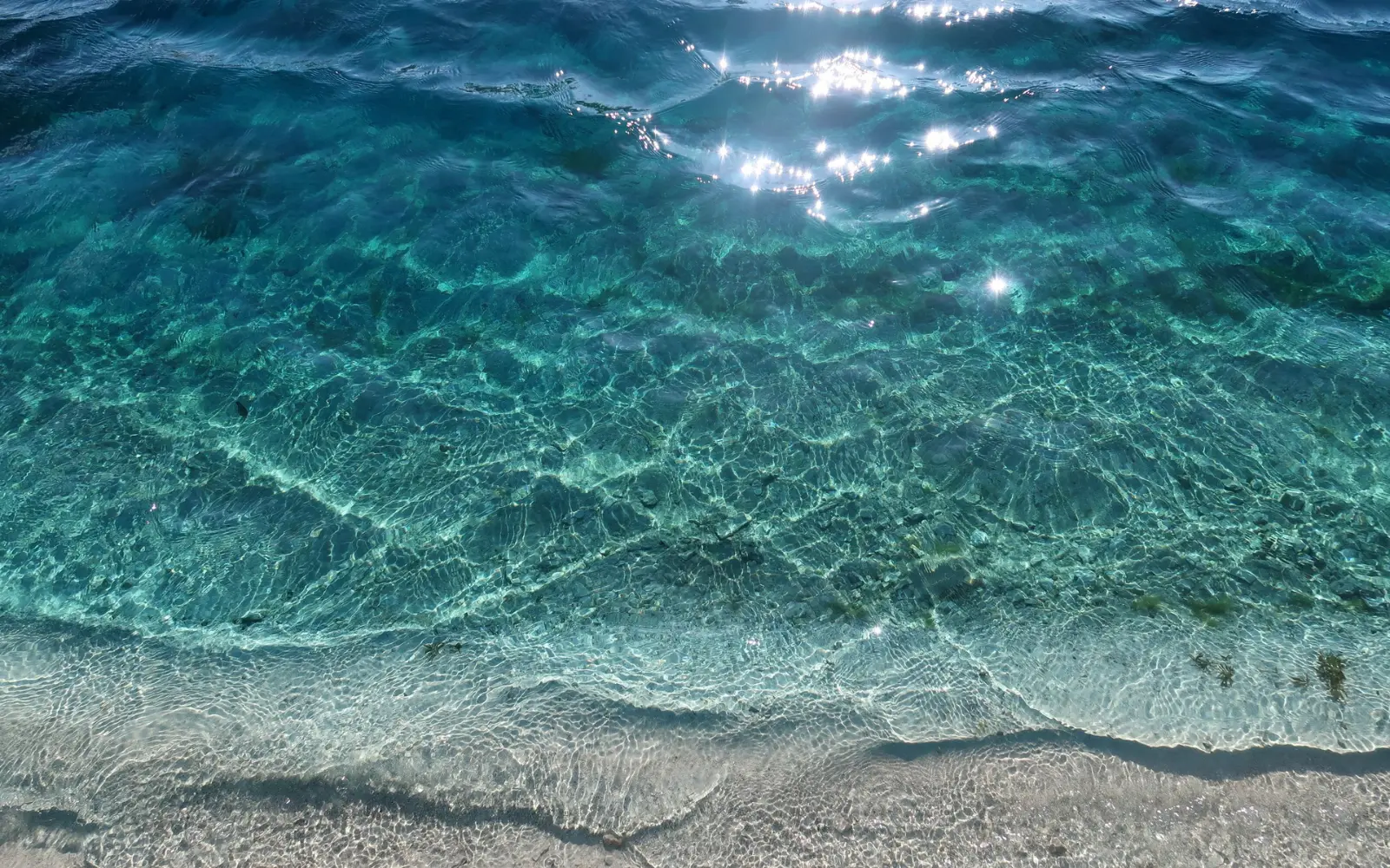 Agua del mar transparente y turquesa llegando con calma a la orilla de arena clara